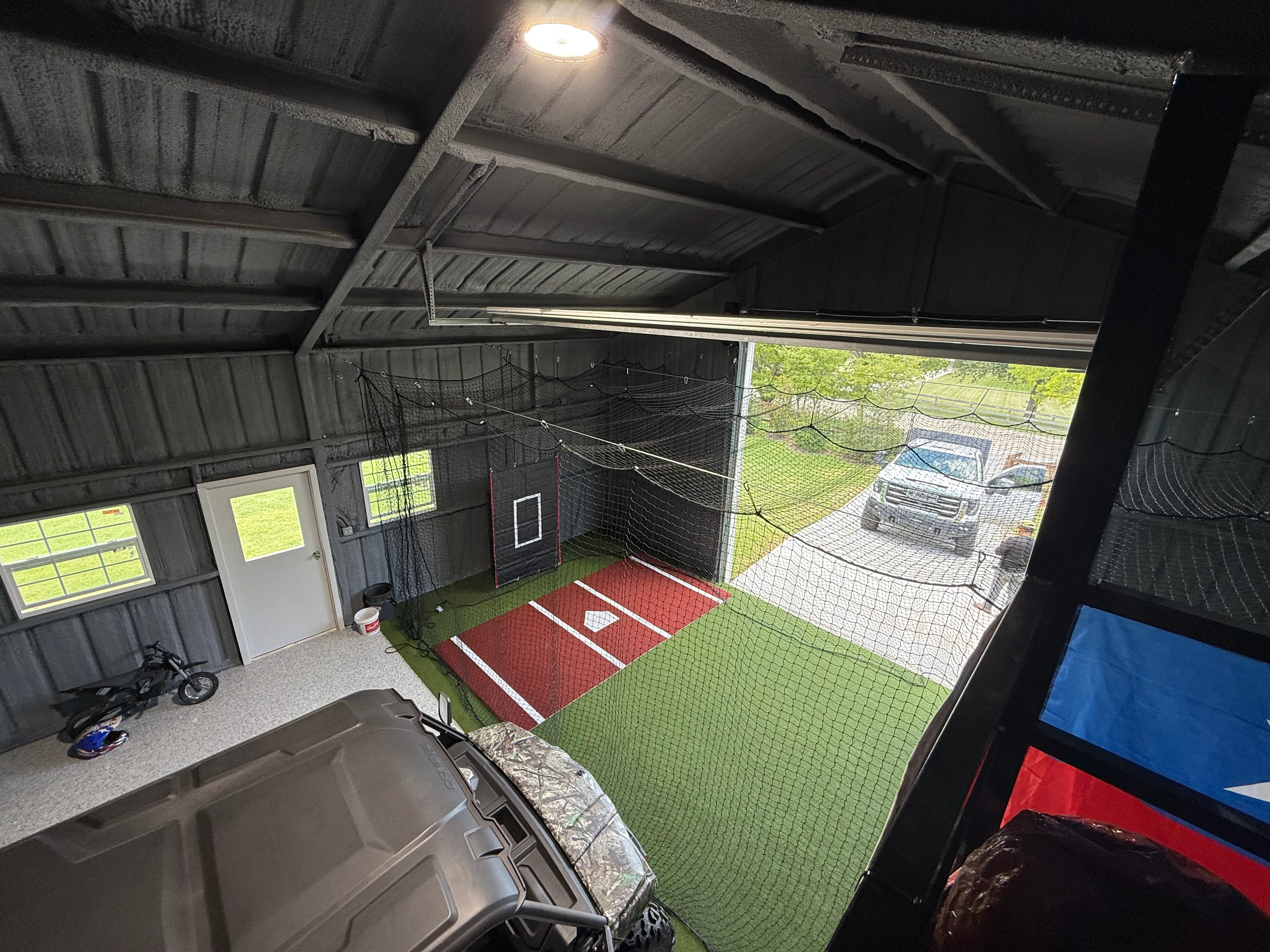 Wide view of a 15x30 batting cage built inside a working barn, nets rigged from the rafters, Argyle TX