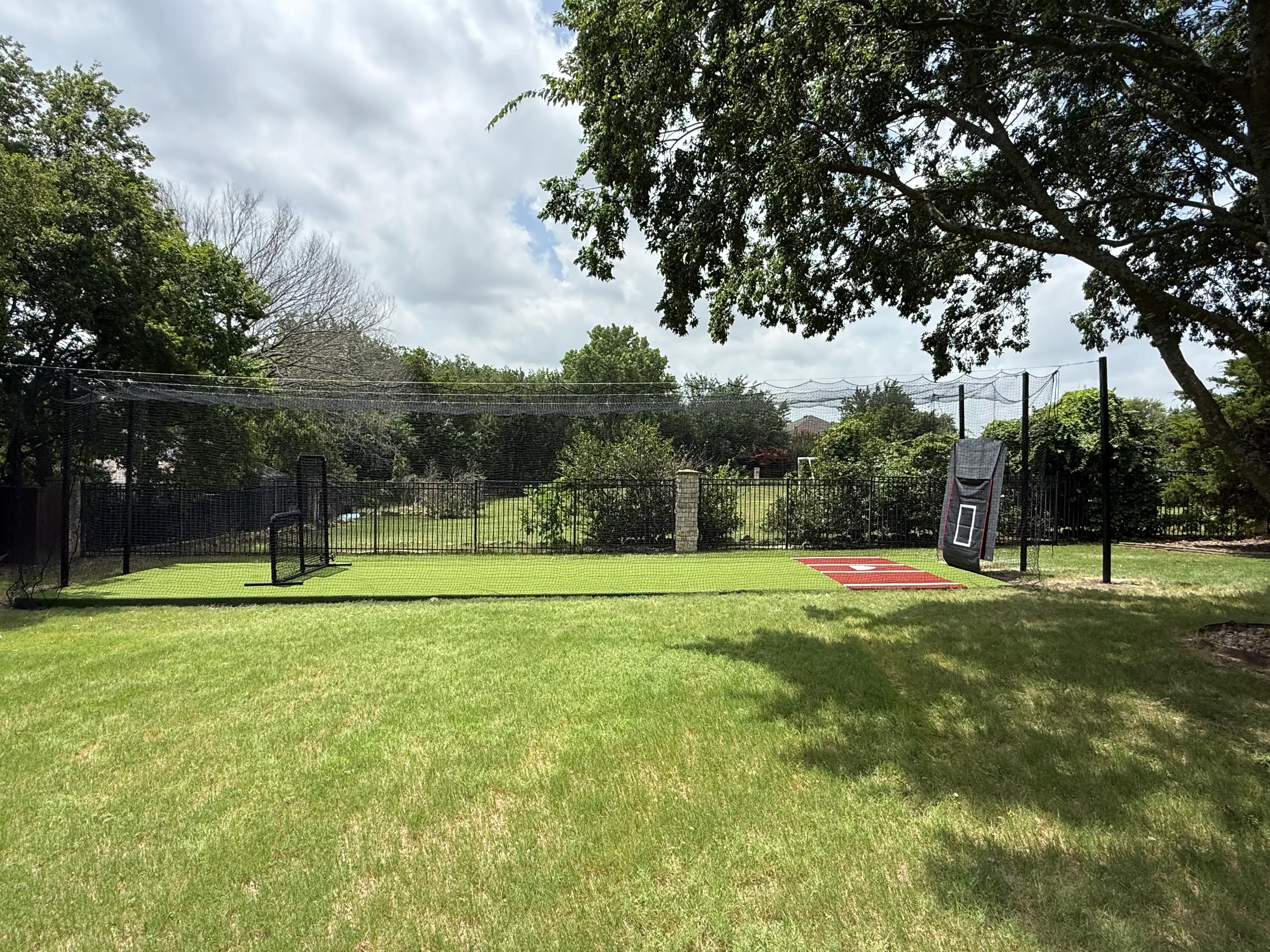 Full-size outdoor batting cage on freestanding steel posts in an Allen, TX backyard, with an L-screen and red turf batter’s box