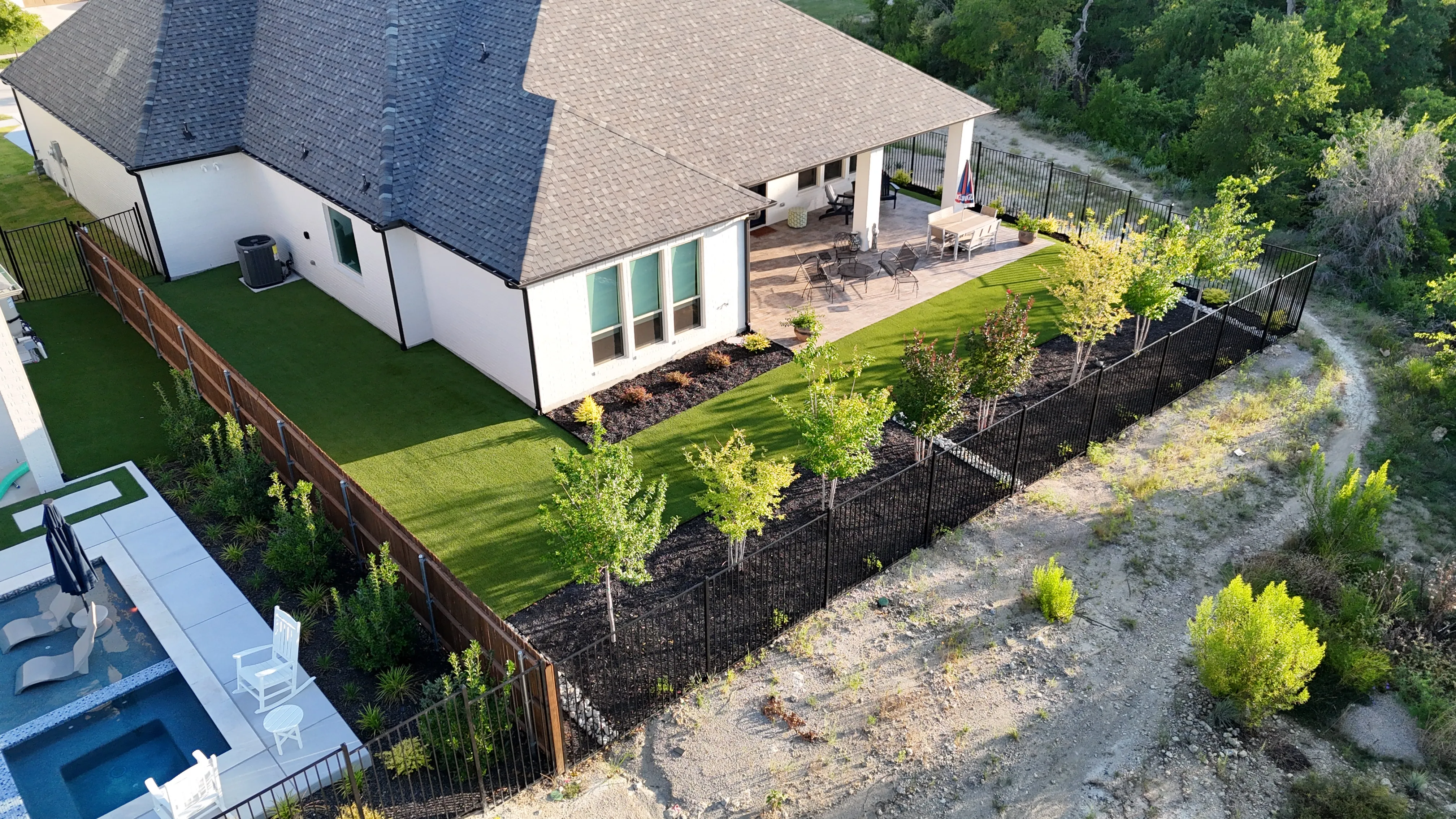 Aerial of a new artificial turf backyard with covered patio, dining set, and freshly planted landscape bed along the fence line in DFW