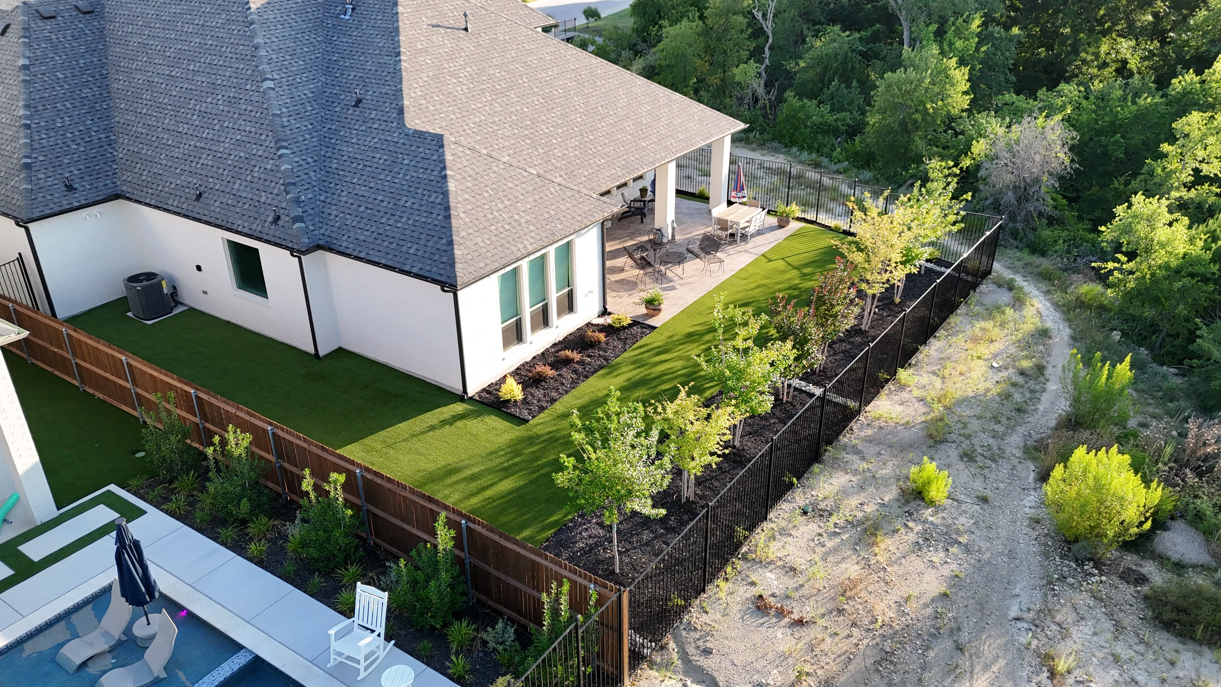 Aerial of a narrow turf side yard running beside a pool with rock waterfall feature in DFW