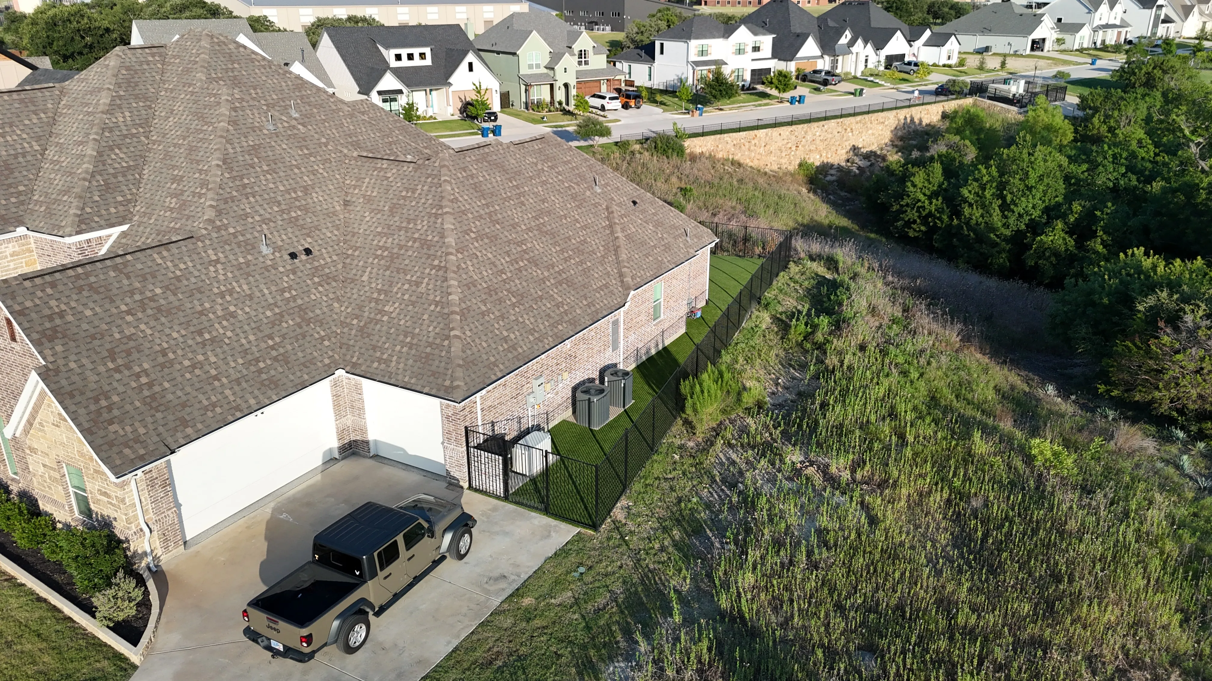 Aerial of a narrow artificial turf strip along a sloped side yard next to a driveway in DFW