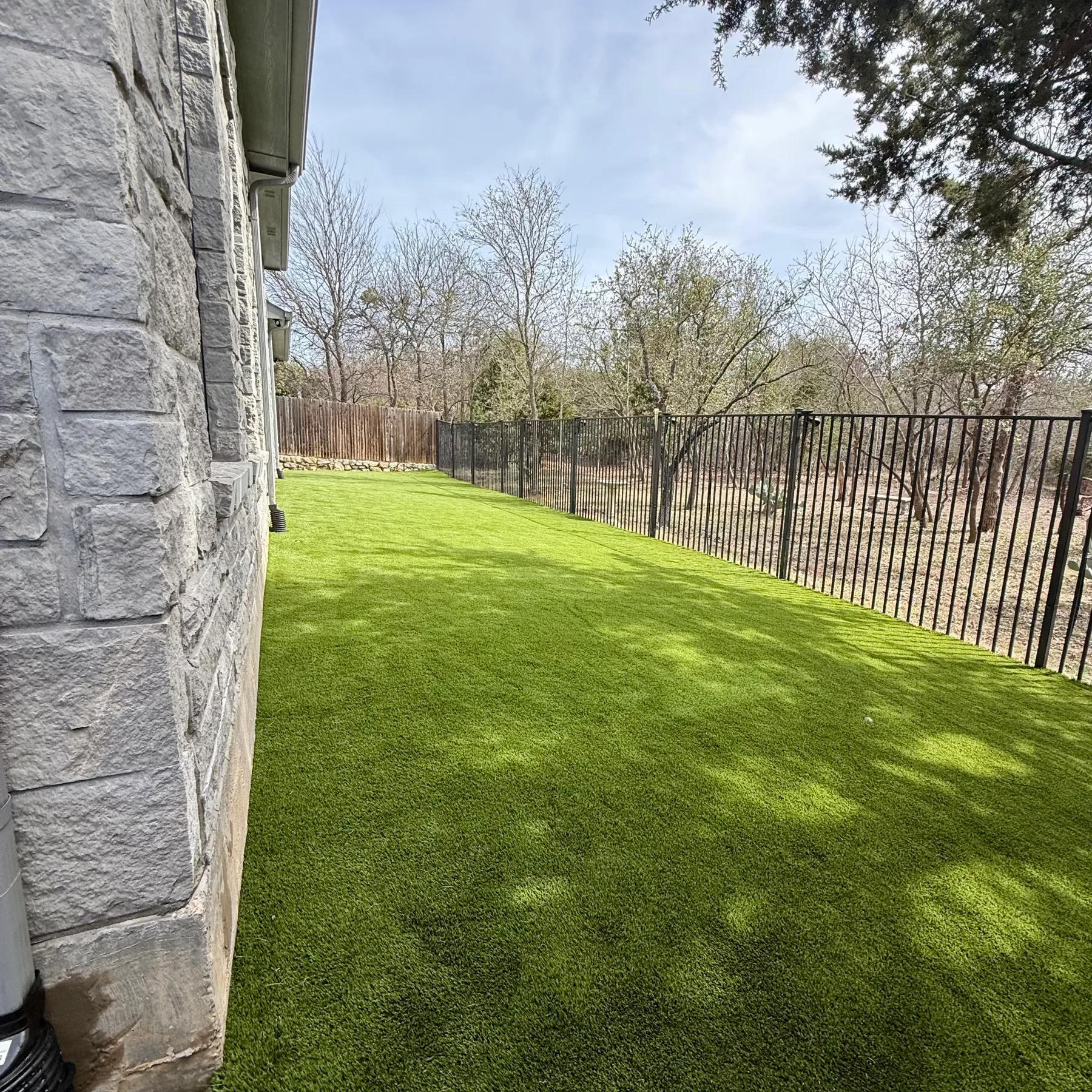 Side-yard artificial turf along stone home foundation in Aledo TX