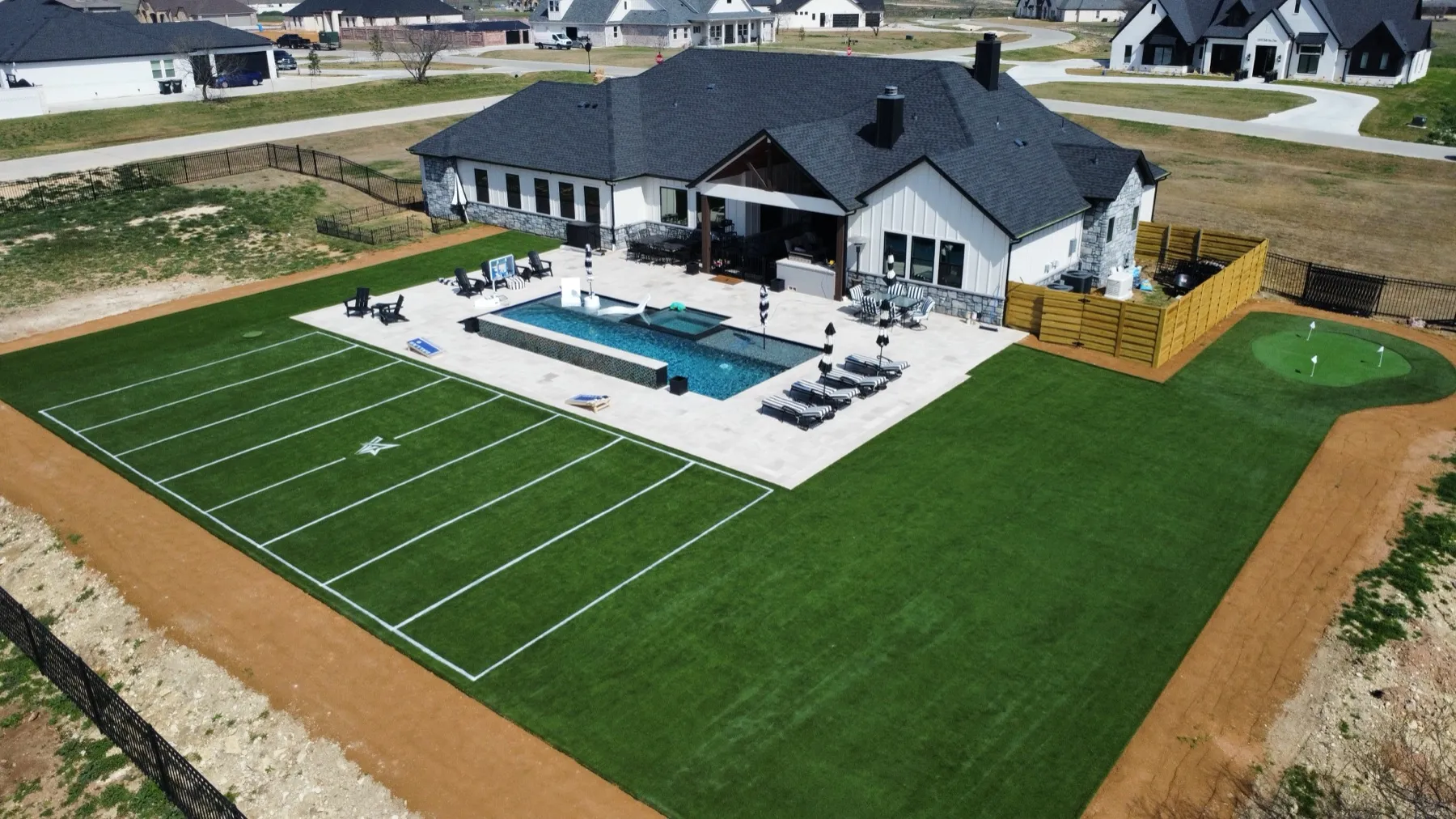 Aerial luxury backyard with football field turf, pool, and putting green