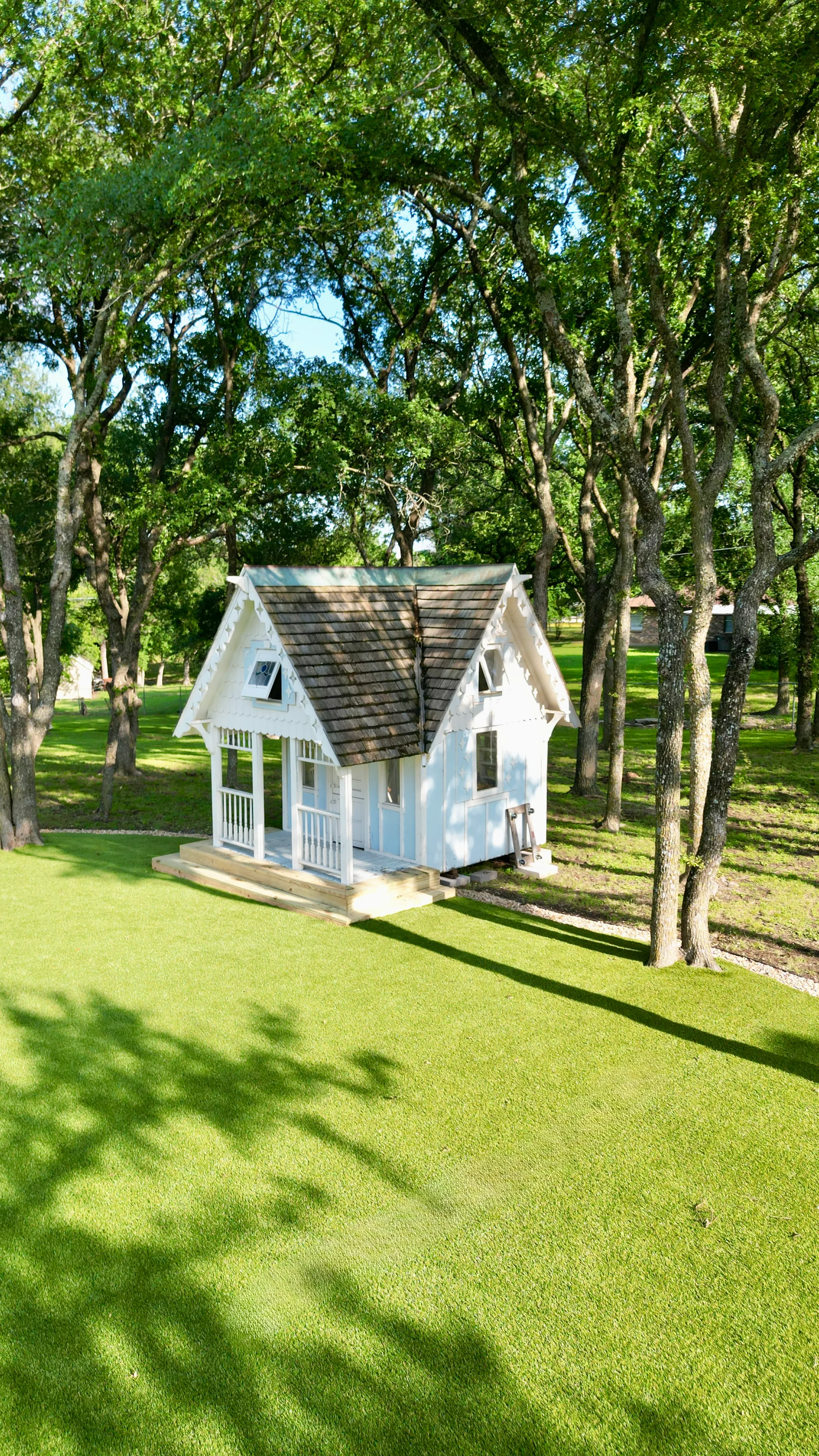 Vertical aerial of artificial turf lawn and kids playhouse under dense oak tree canopy in DFW