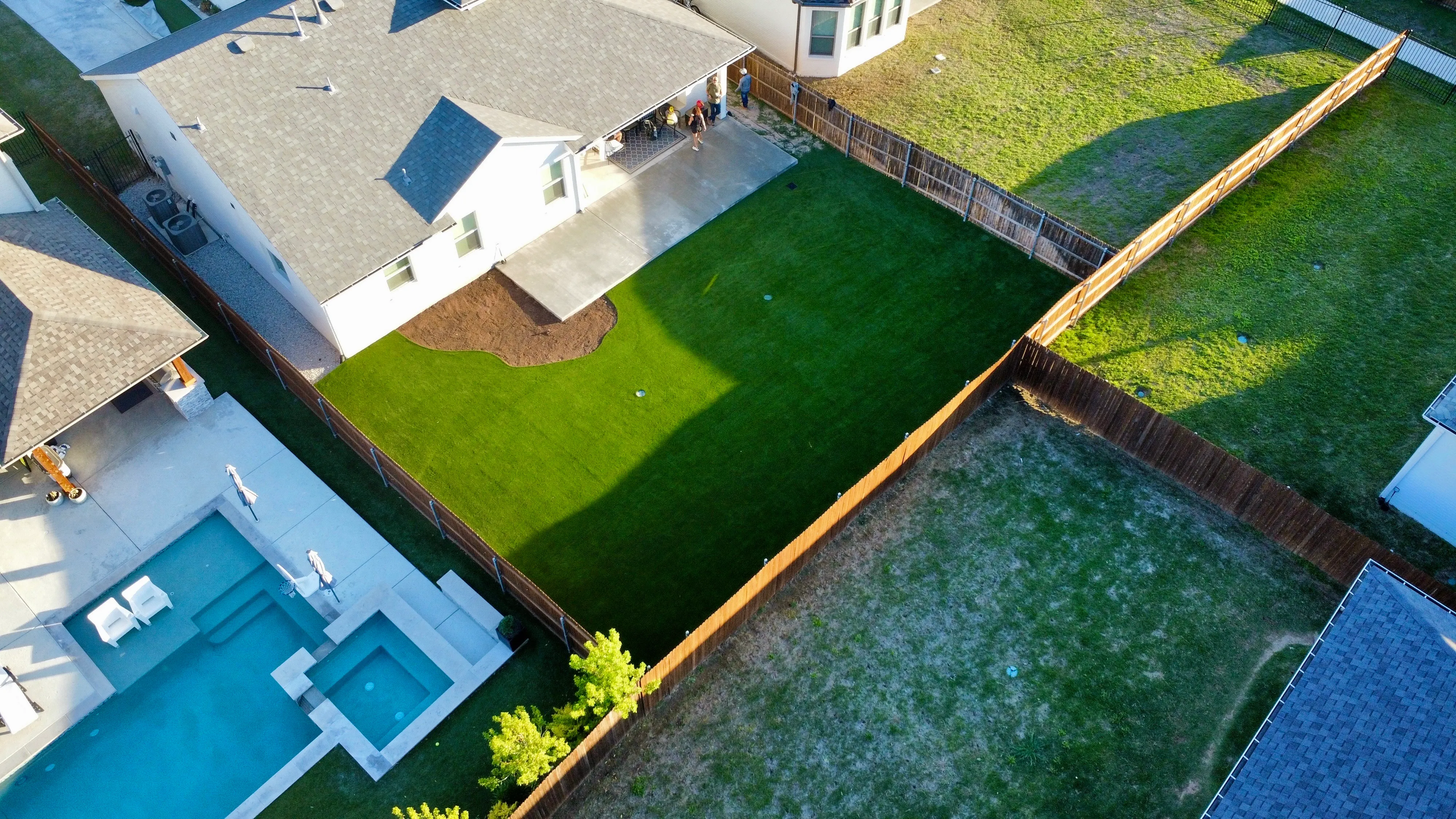 Aerial comparison of vivid green artificial turf backyard against a neighboring lot of dormant brown natural grass in DFW