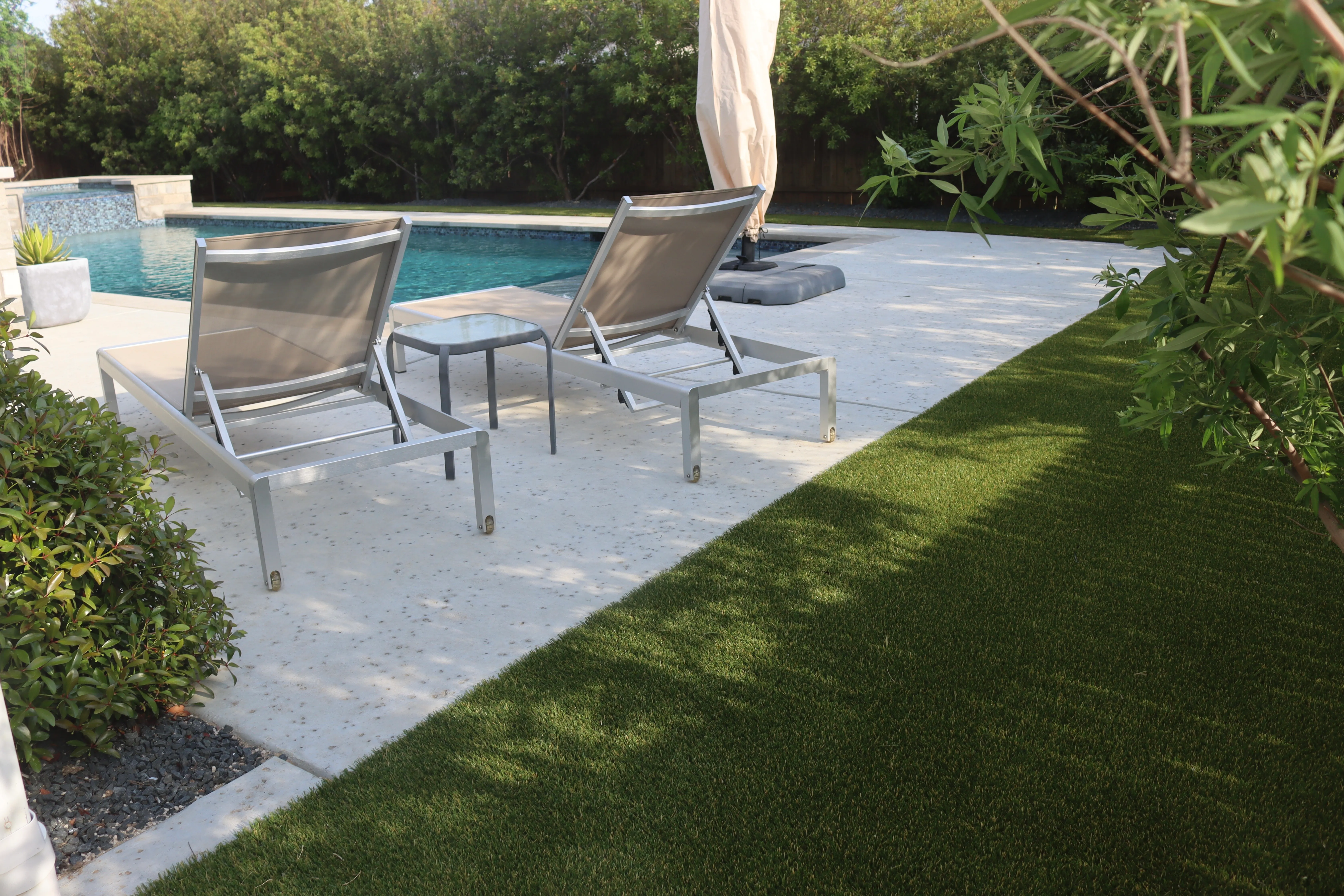 Artificial turf lawn beside a pool with rock waterfall feature and lounge chairs in a DFW backyard