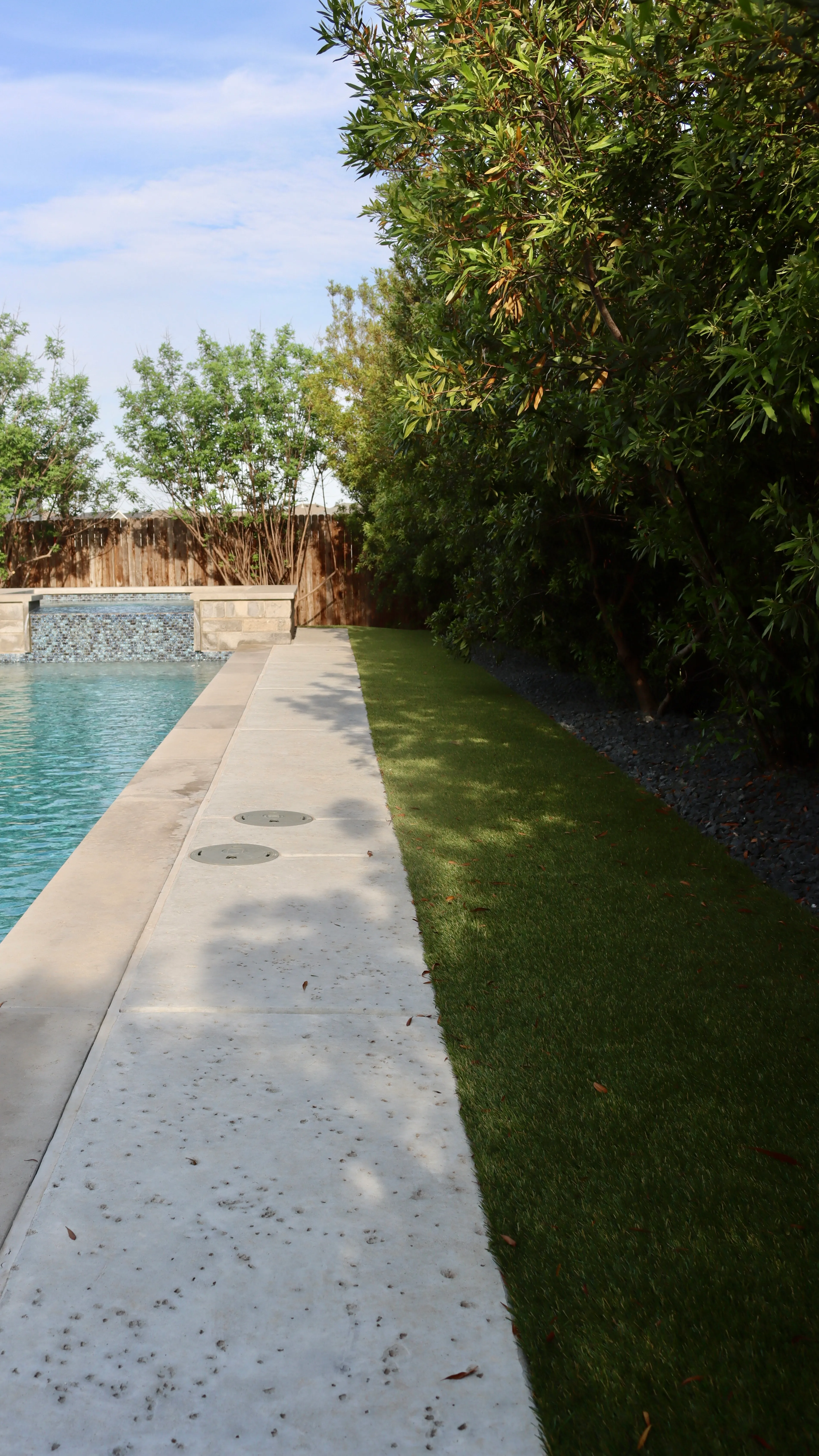 Narrow artificial turf strip along a pool edge with stone coping in a DFW backyard