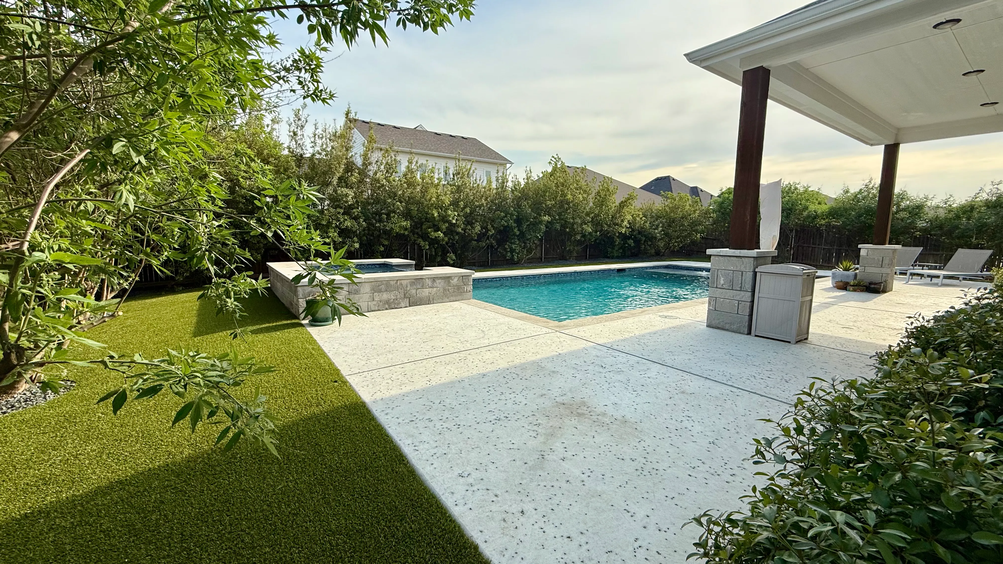 Backyard pool with raised square spa and wood pergola patio bordered by artificial turf in DFW