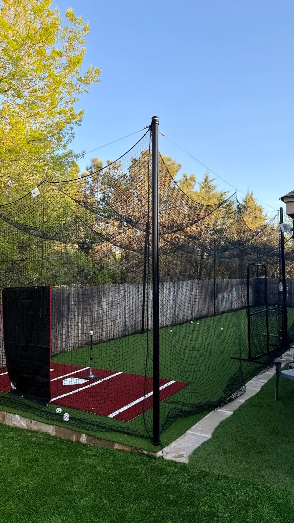 Empty backyard batting cage with red turf home plate, black netting, and steel poles in Aledo TX