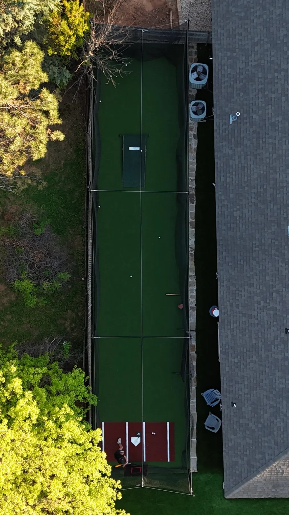 Overhead drone view of backyard batting cage with green turf, red home plate mat, and netting beside Aledo TX home