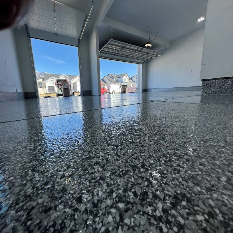 Ground-level view of a dark gray flake epoxy garage floor coating with open bay doors and mountain view in DFW