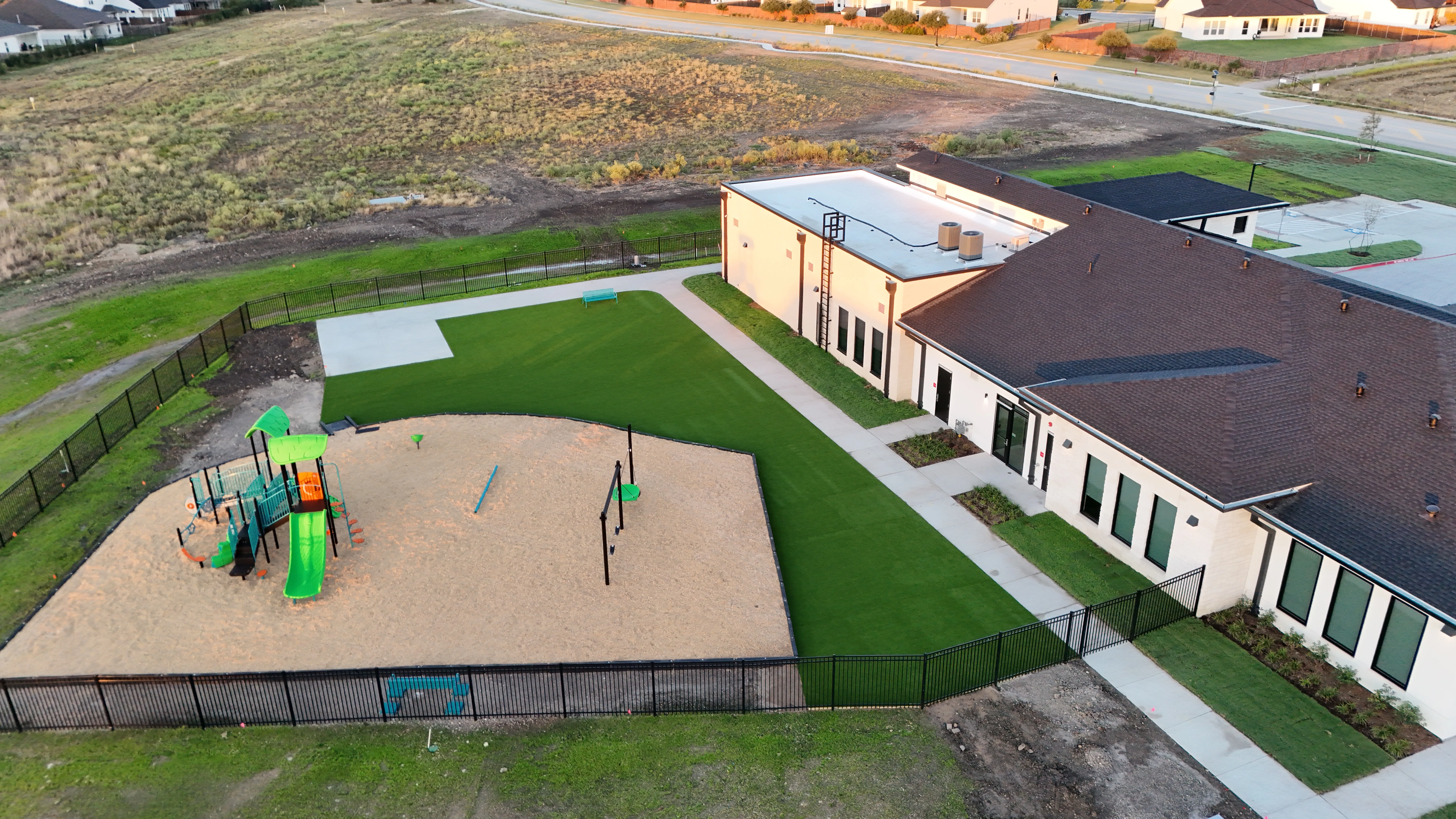 Aerial of a school playground with a sand play area, play structure, and artificial turf field beside the school building