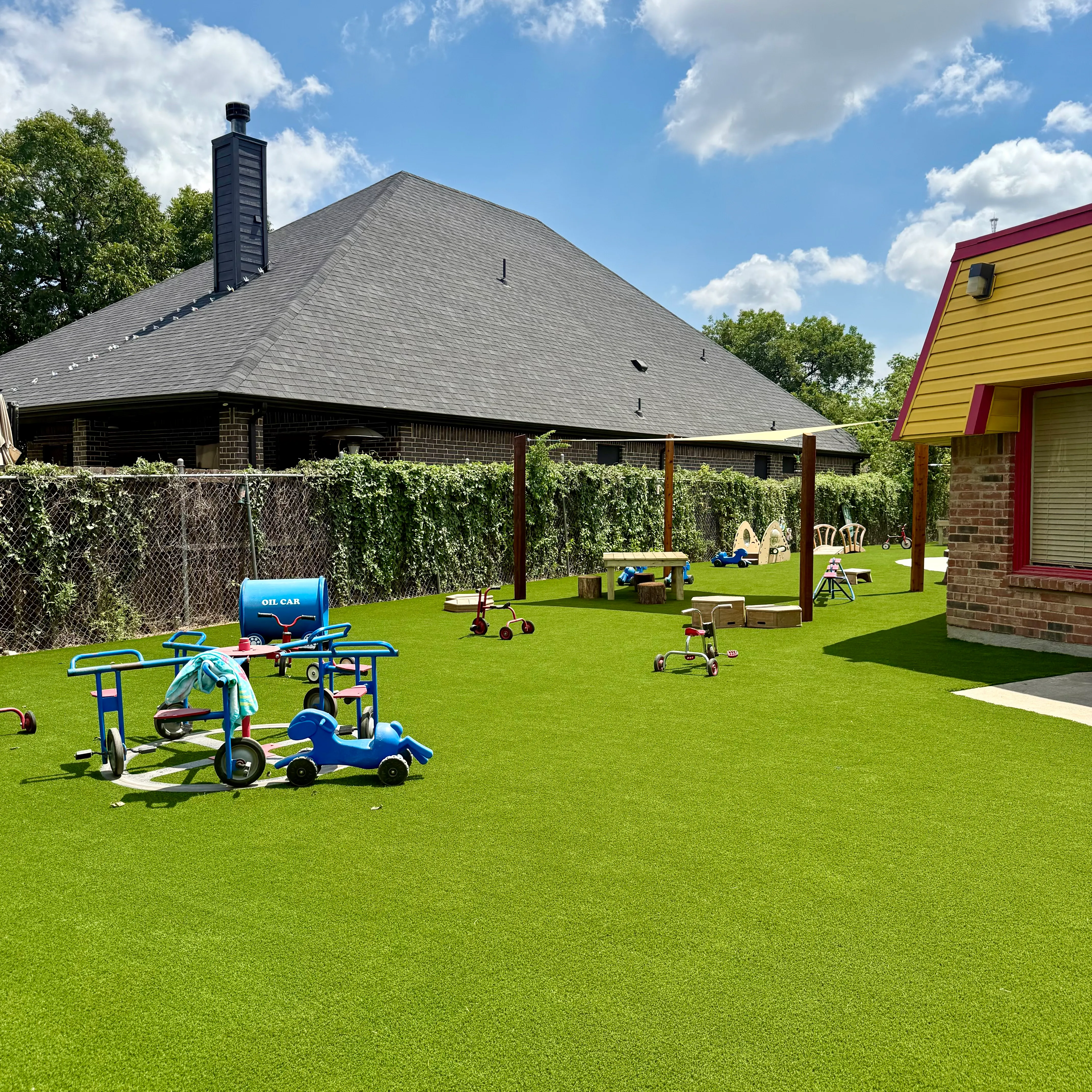 Elevated view of a school playground with a green play structure in a sand pit beside a turf field and brick school building