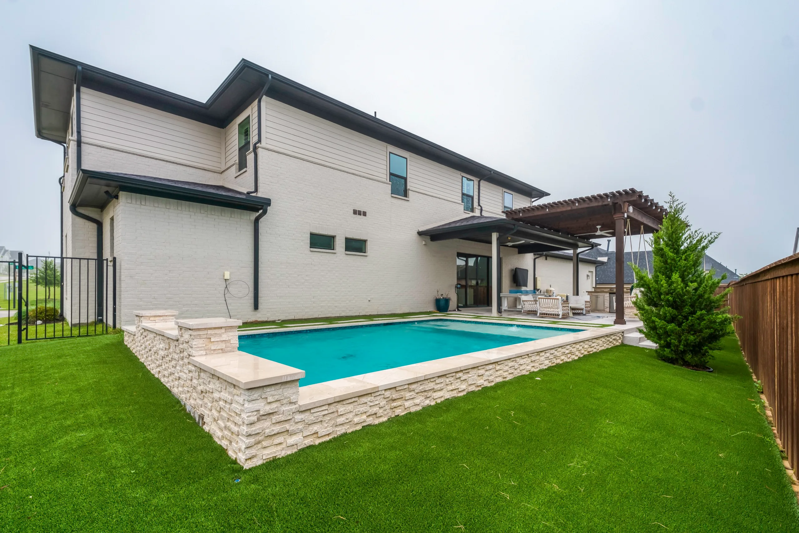 Modern backyard pool with stacked-stone wall and artificial turf