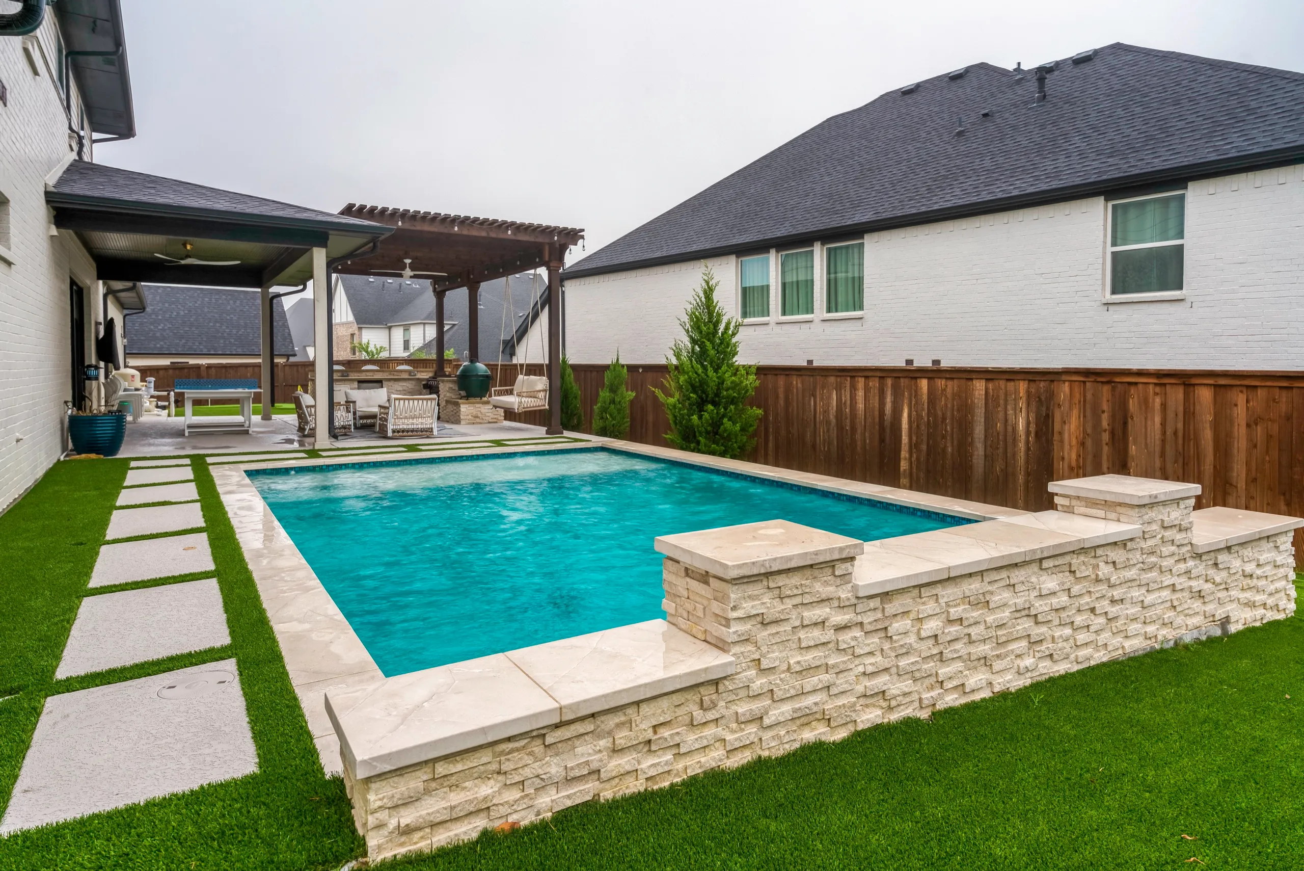 Modern backyard pool with stacked-stone wall and artificial turf