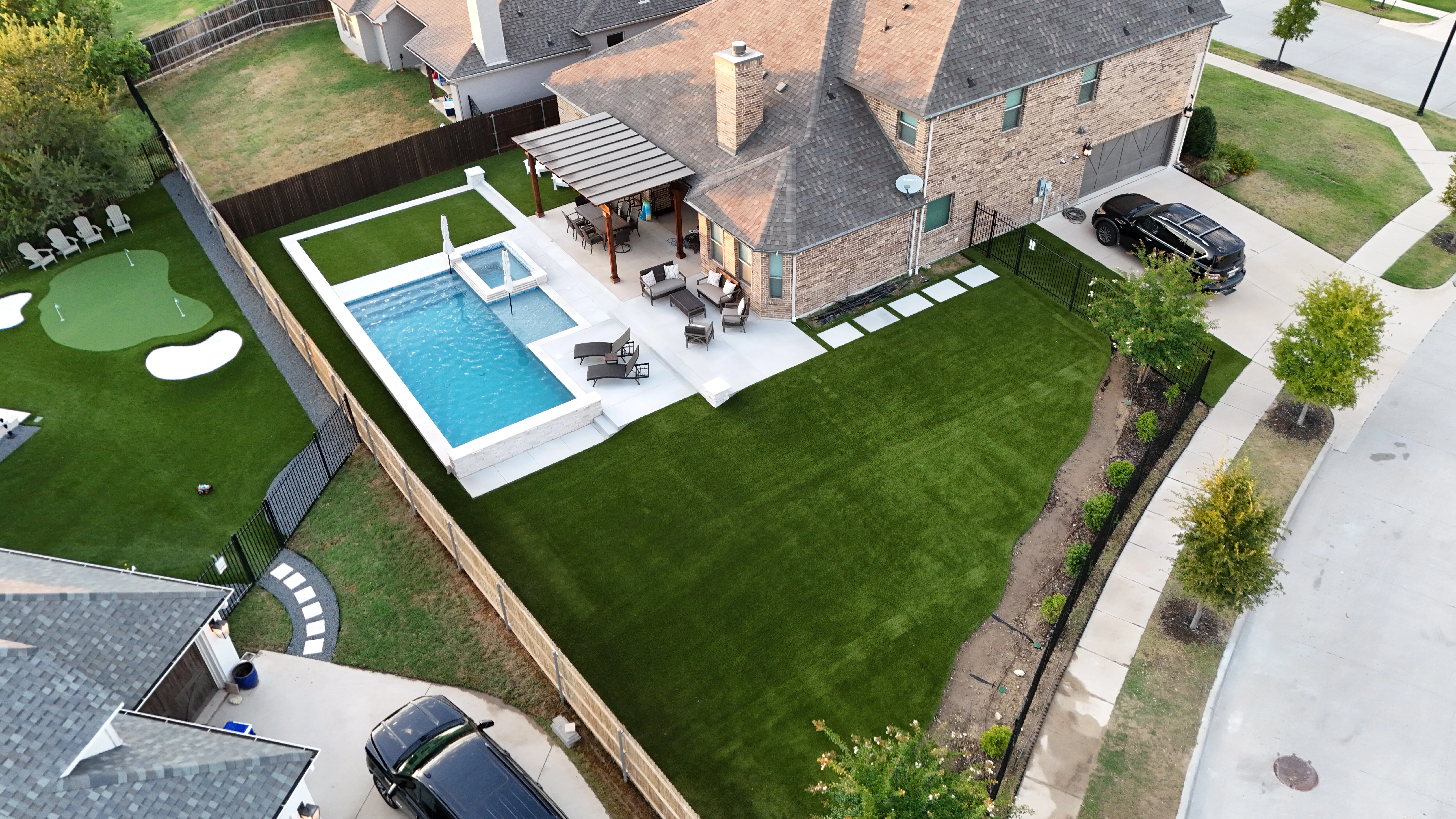 Aerial of a large DFW estate backyard with pool, spa, pergola patio, artificial turf lawn, and a neighboring putting green