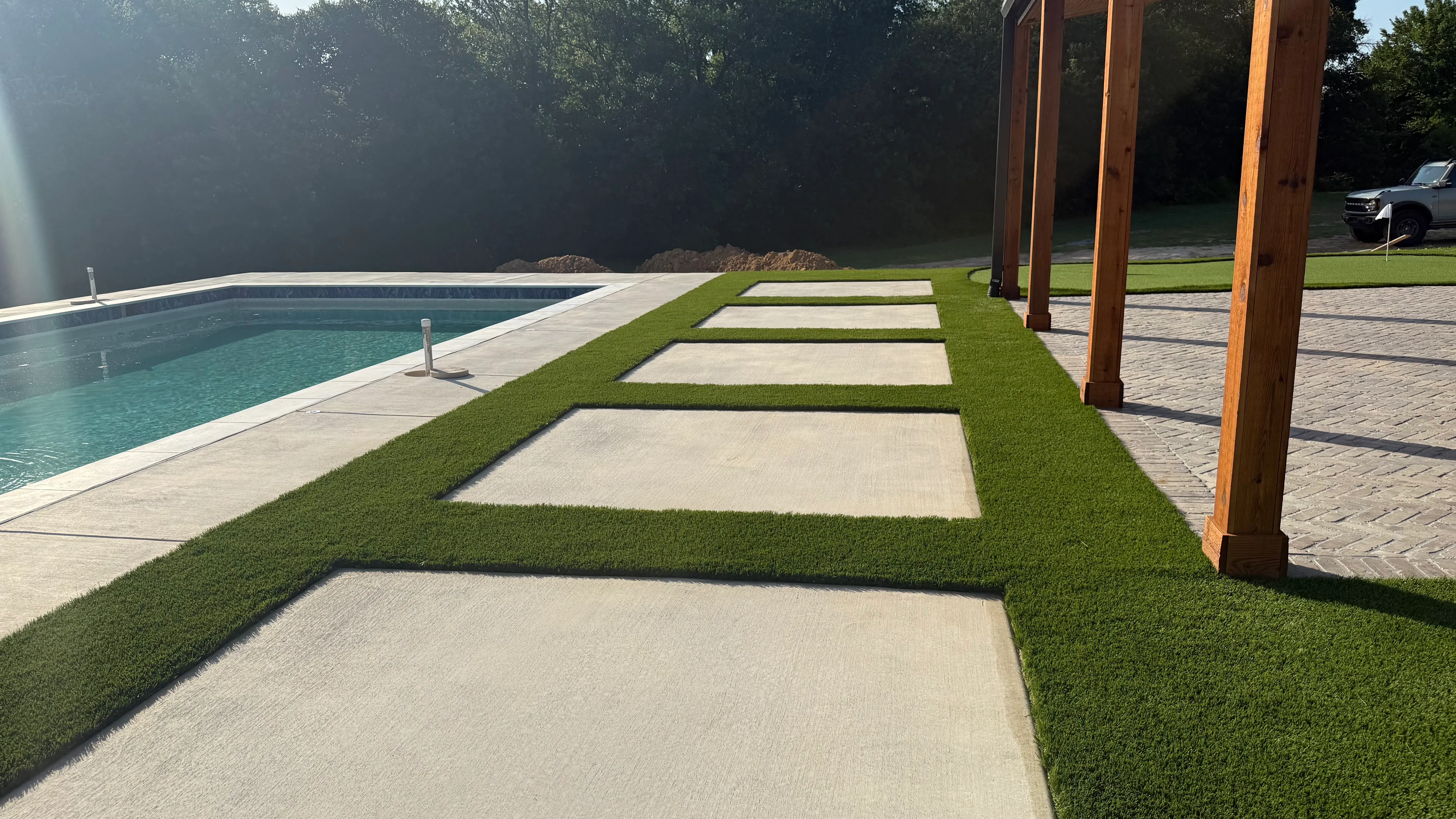 Checkerboard pattern of turf and concrete pavers leading to a modern black barn-style home with putting green and pool in DFW