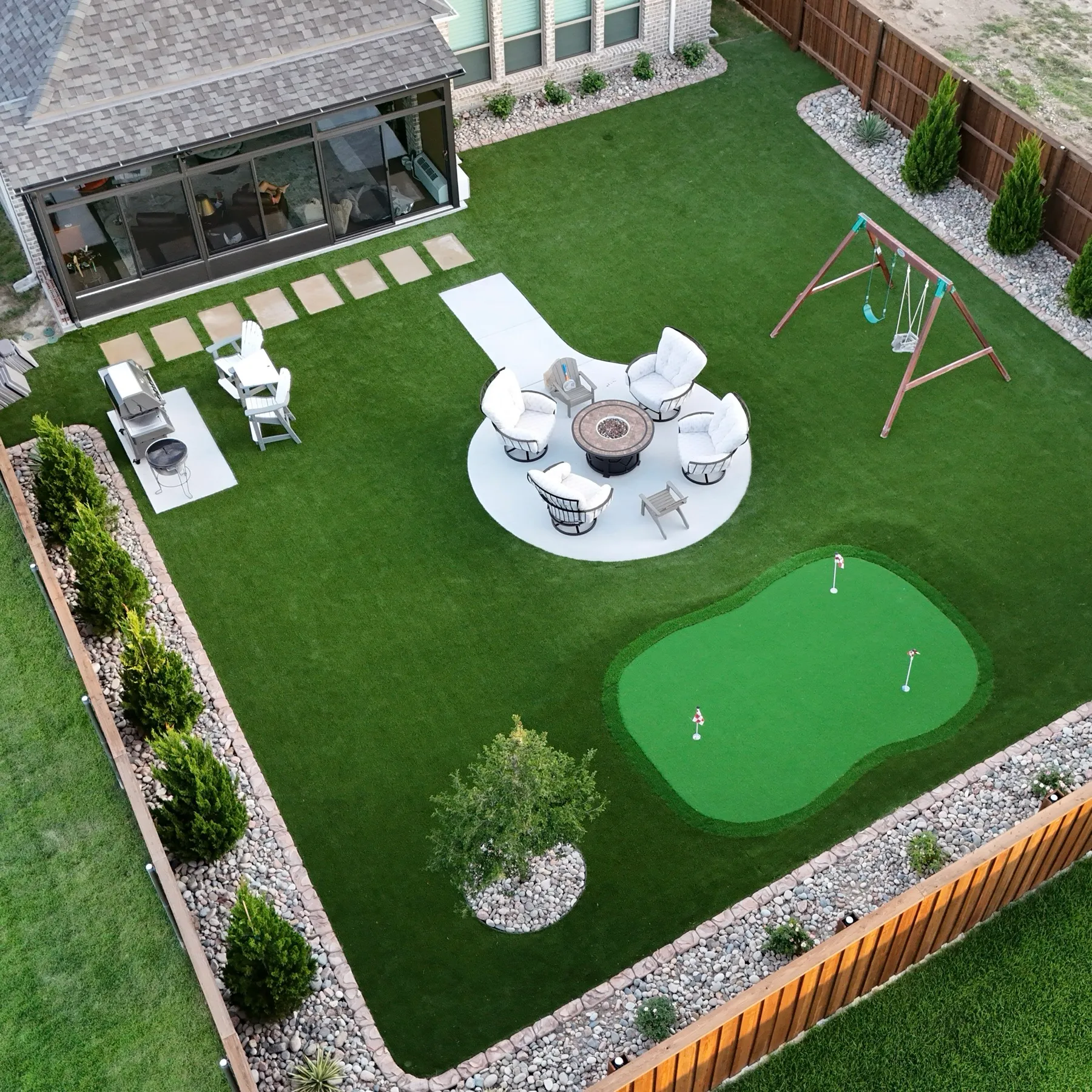 Aledo TX backyard with artificial turf, putting green, fire pit lounge, and playset