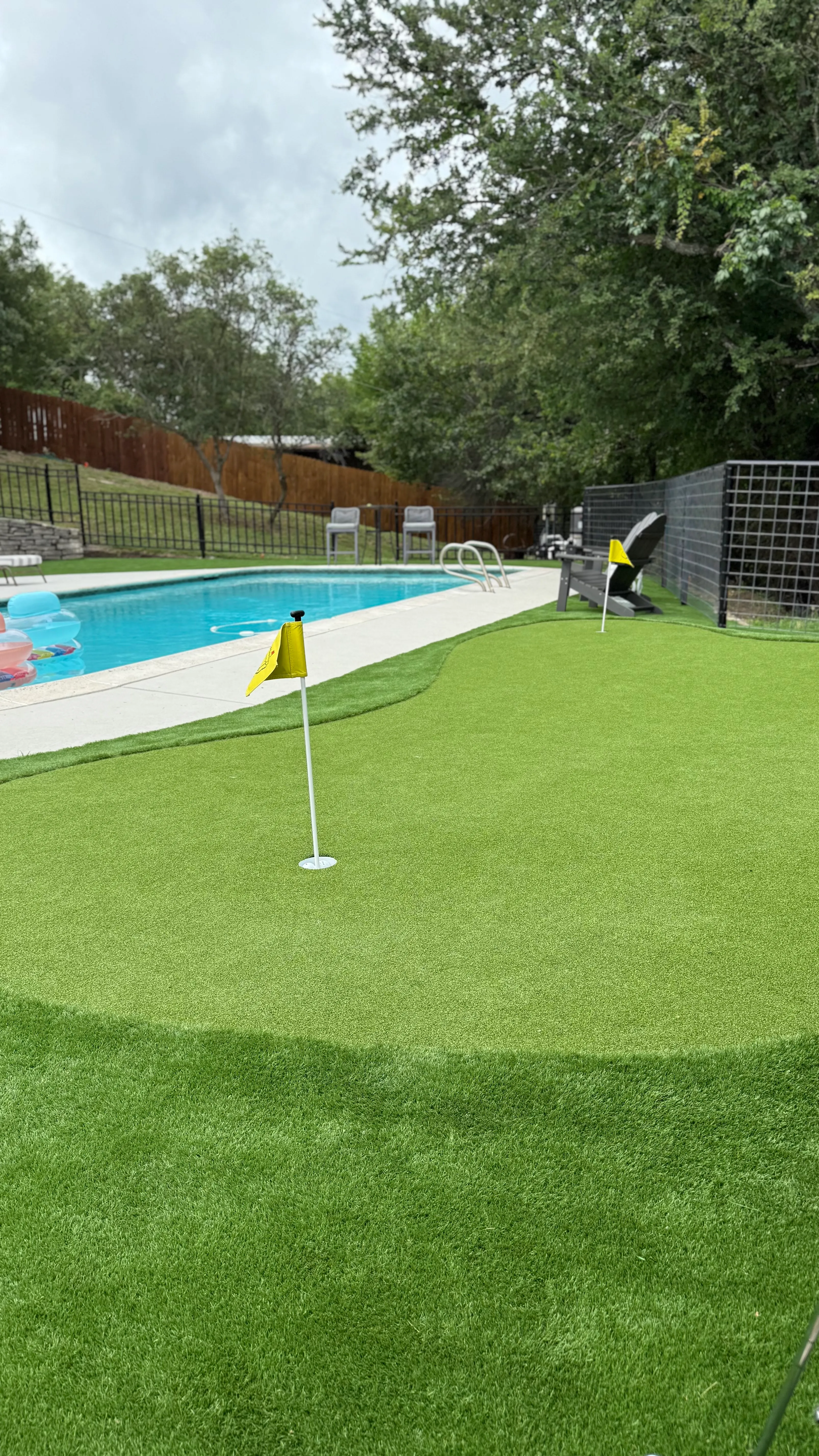 Putting green hole with cup and flag beside a backyard pool in DFW