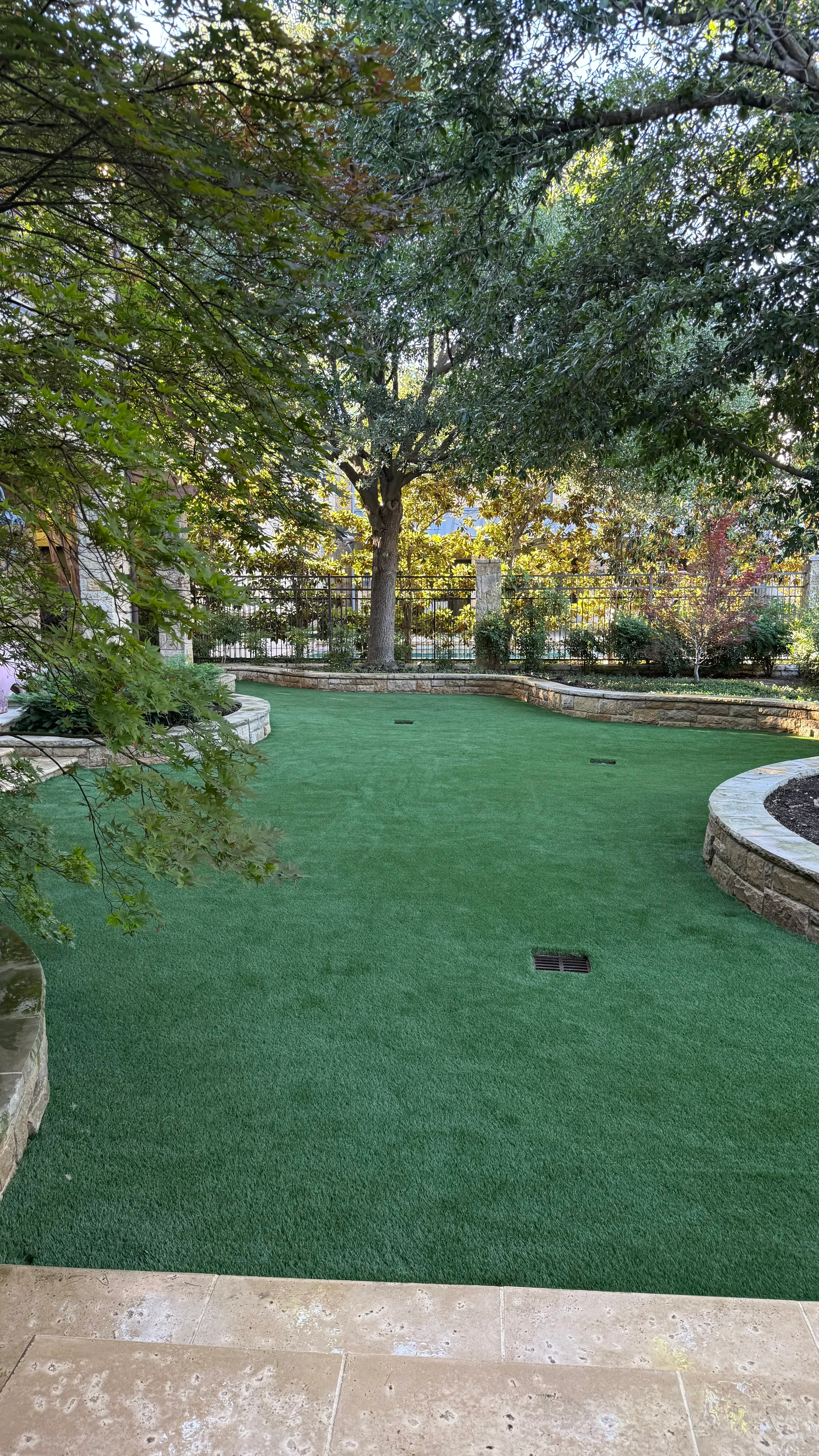 Putting green framed by a stone patio archway with outdoor dining table and chairs in the foreground at a DFW estate