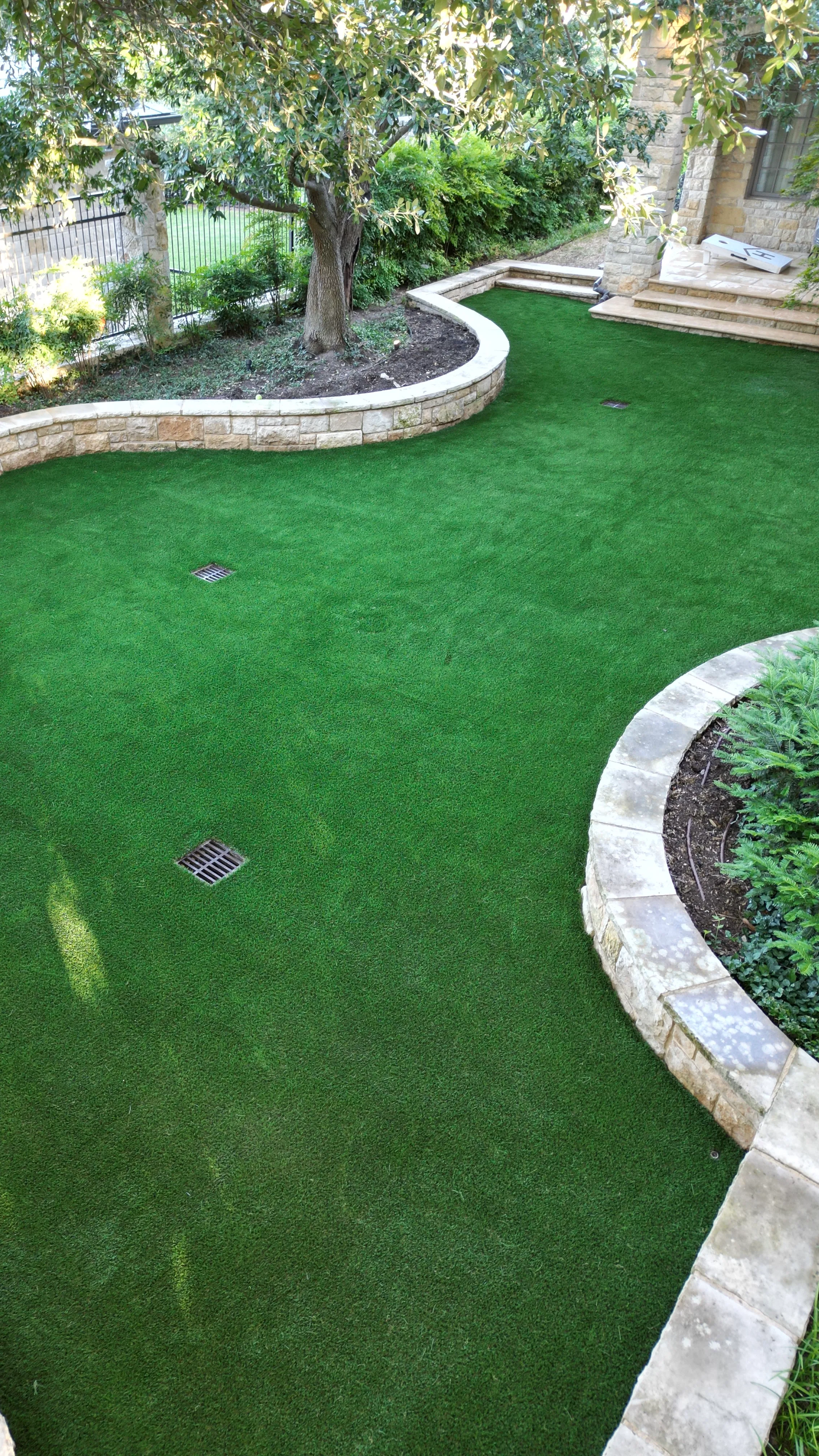 Aerial view of a backyard putting green curving past stone retaining walls and landscaped beds in DFW