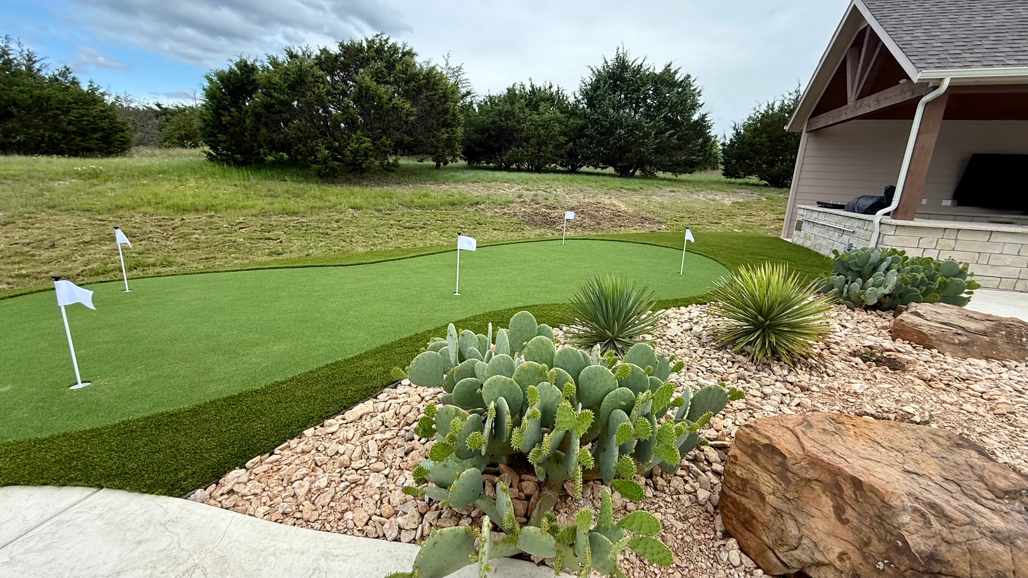 Curved putting green with four flags beside a xeriscape rock bed of cactus and yucca at a Texas Hill Country home