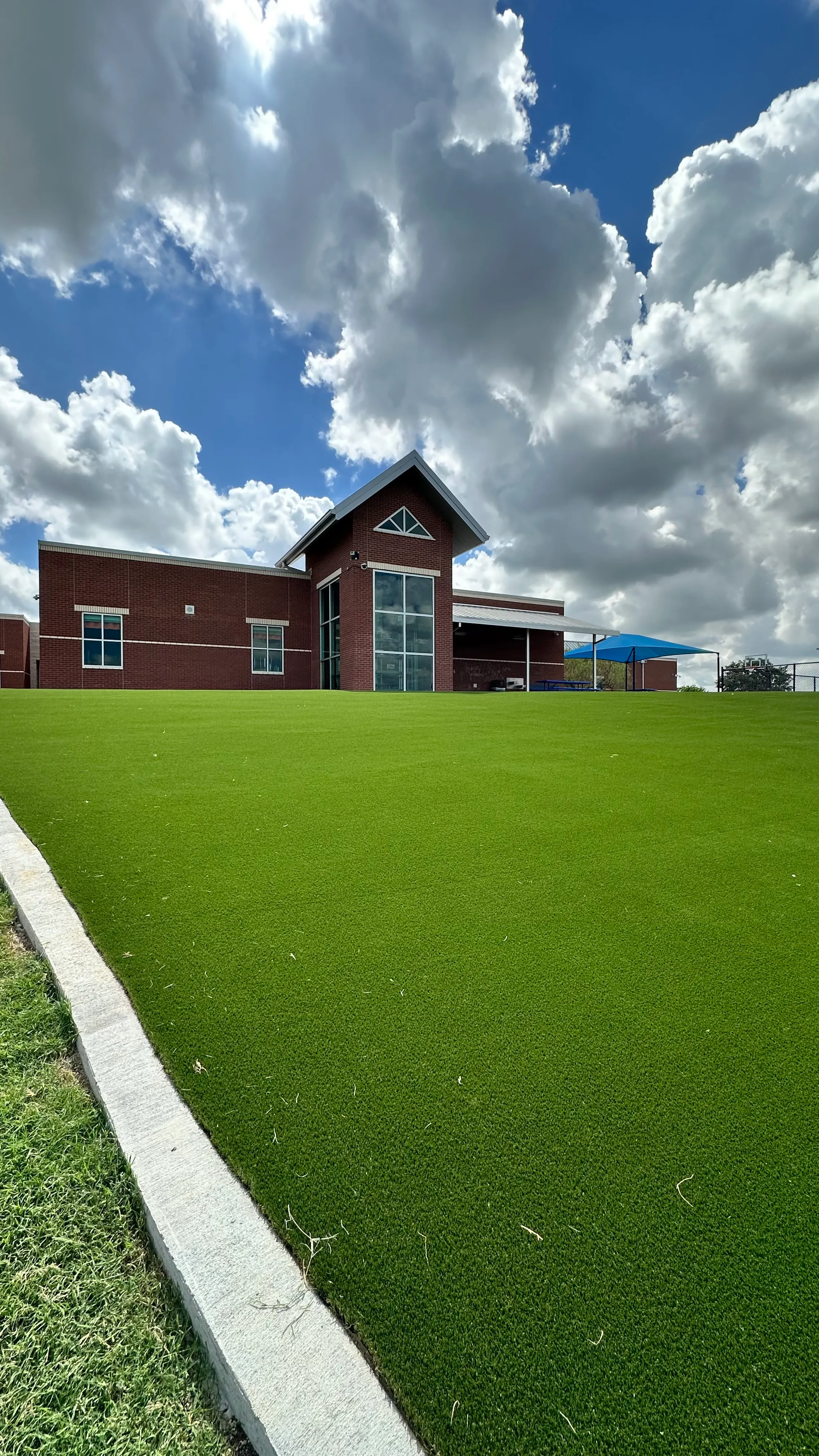 Ground-level view of a sloped artificial turf field leading up to a red brick elementary school building with a covered walkway