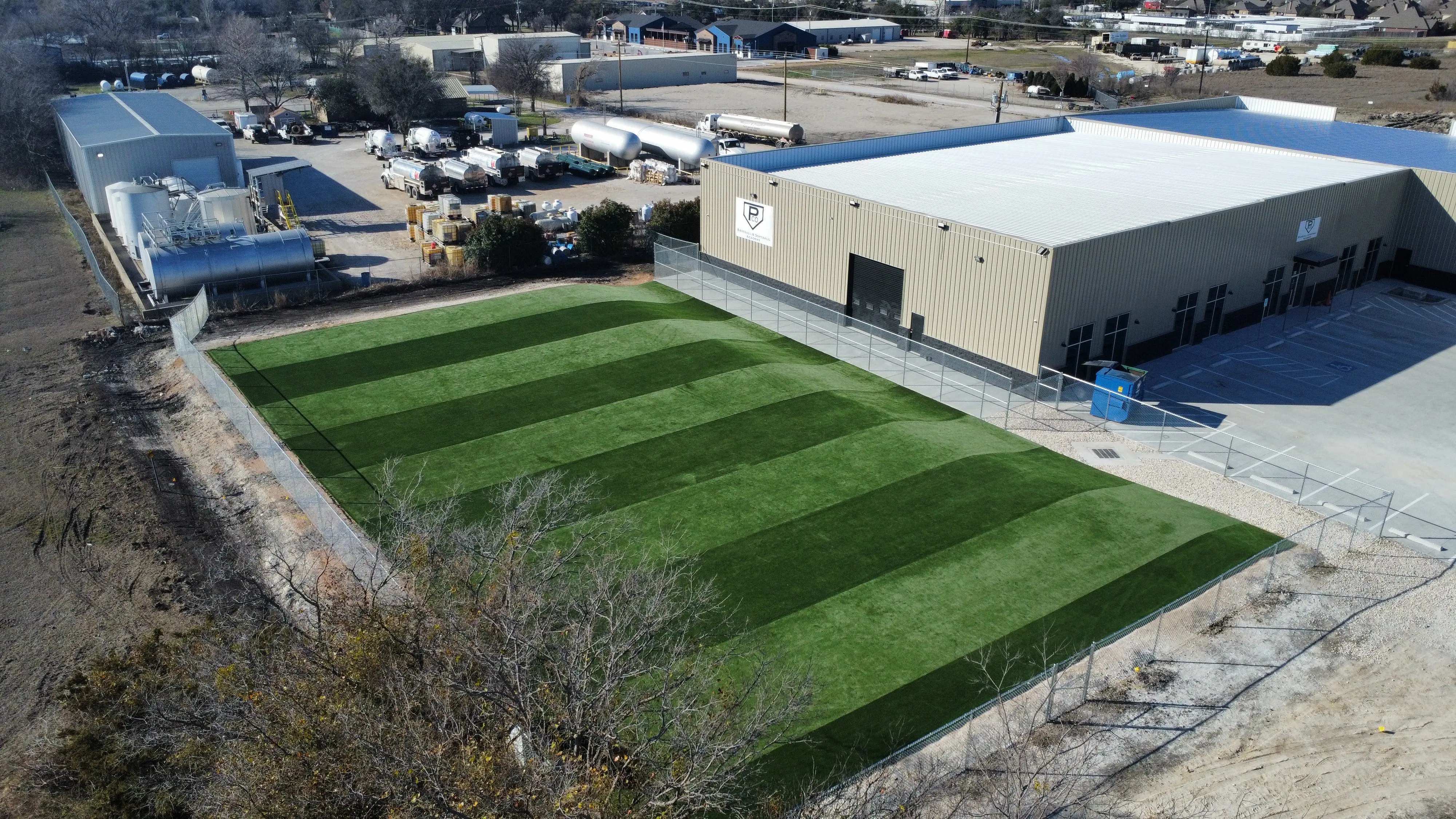 Aerial of striped commercial artificial turf training field beside Parker County Baseball & Softball Academy building in DFW