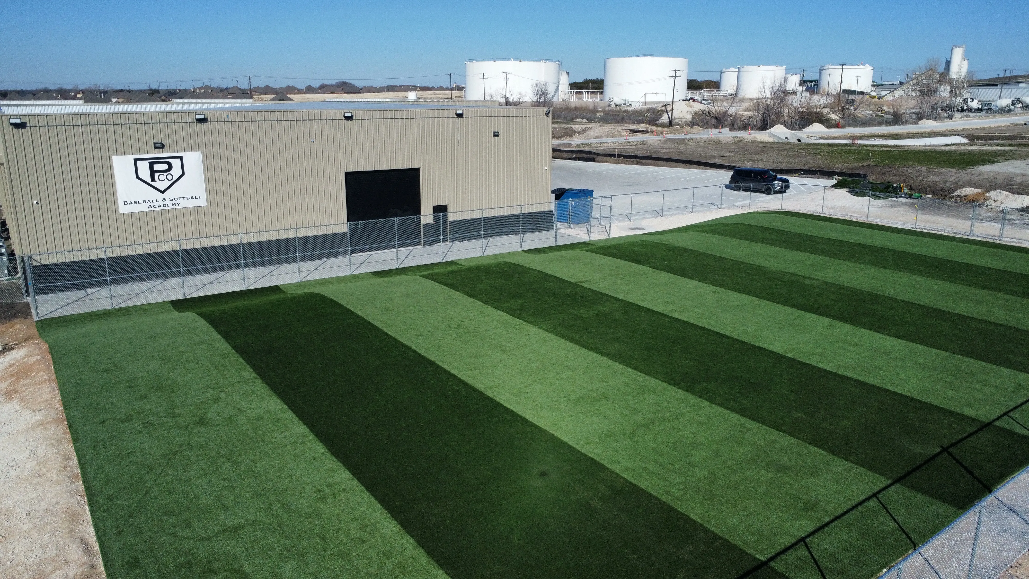 Elevated view of striped commercial turf field at Parker County Baseball & Softball Academy with industrial DFW backdrop