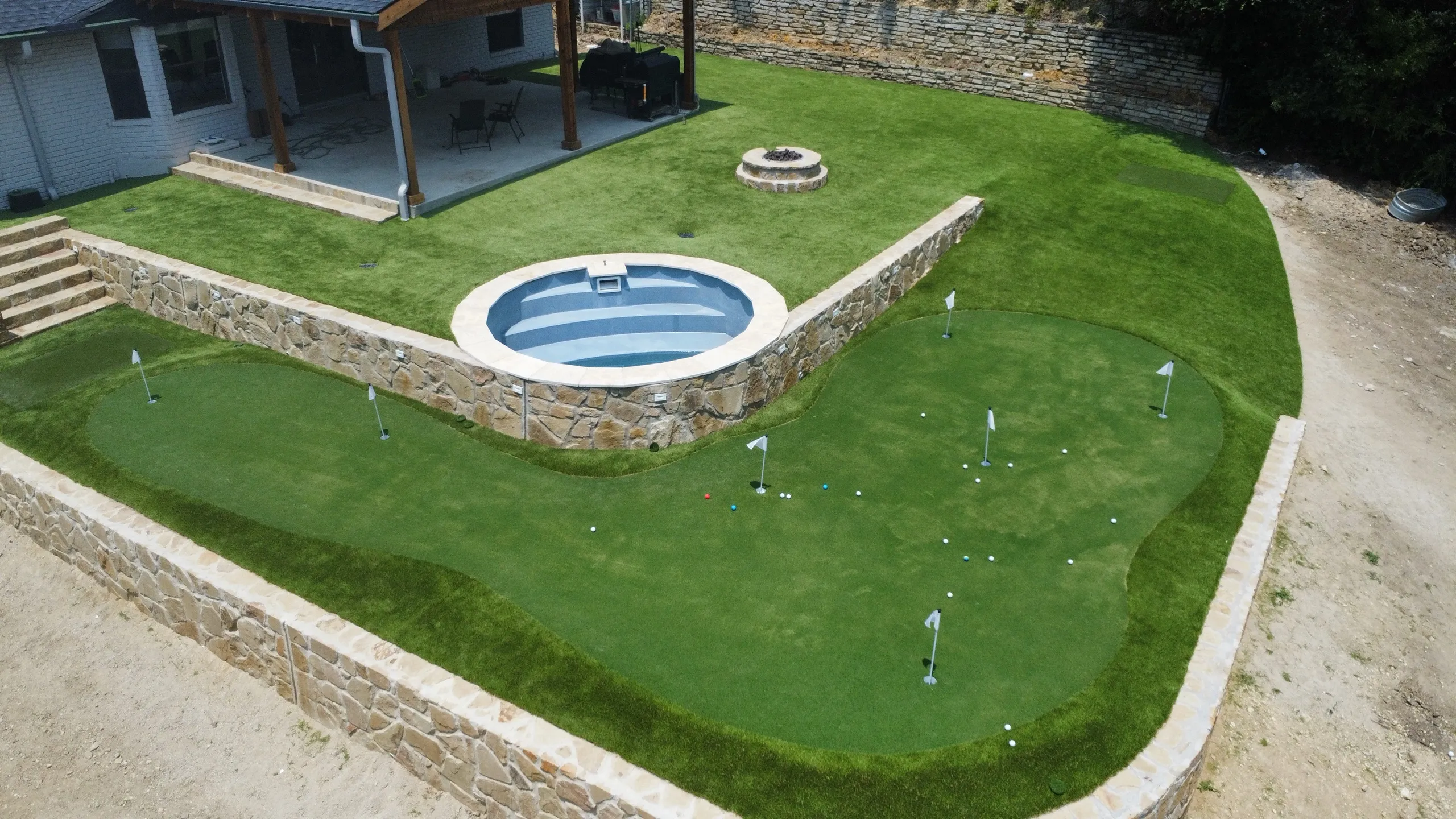 Aerial view of a Bearcat Turf & Outdoors backyard putting green with firepit and stock-tank pool in Parker County