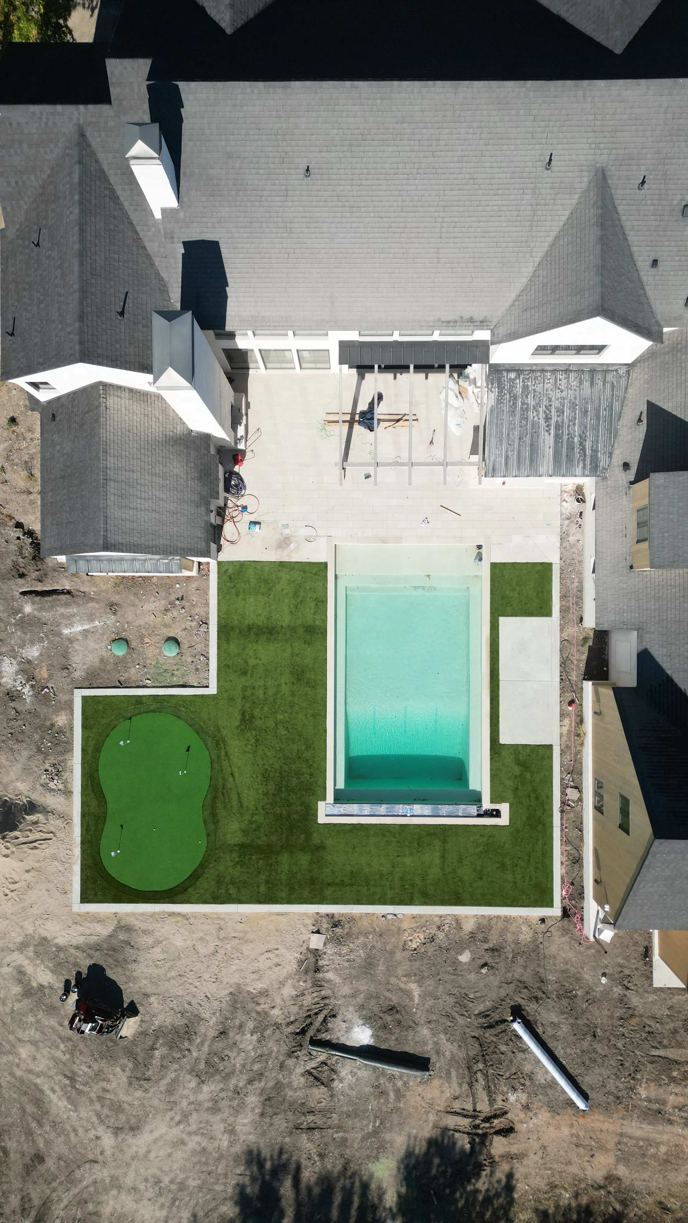 Aerial view of the finished Pecan Plantation backyard: artificial turf lawn surrounding a pool and a custom putting green with multiple flags.