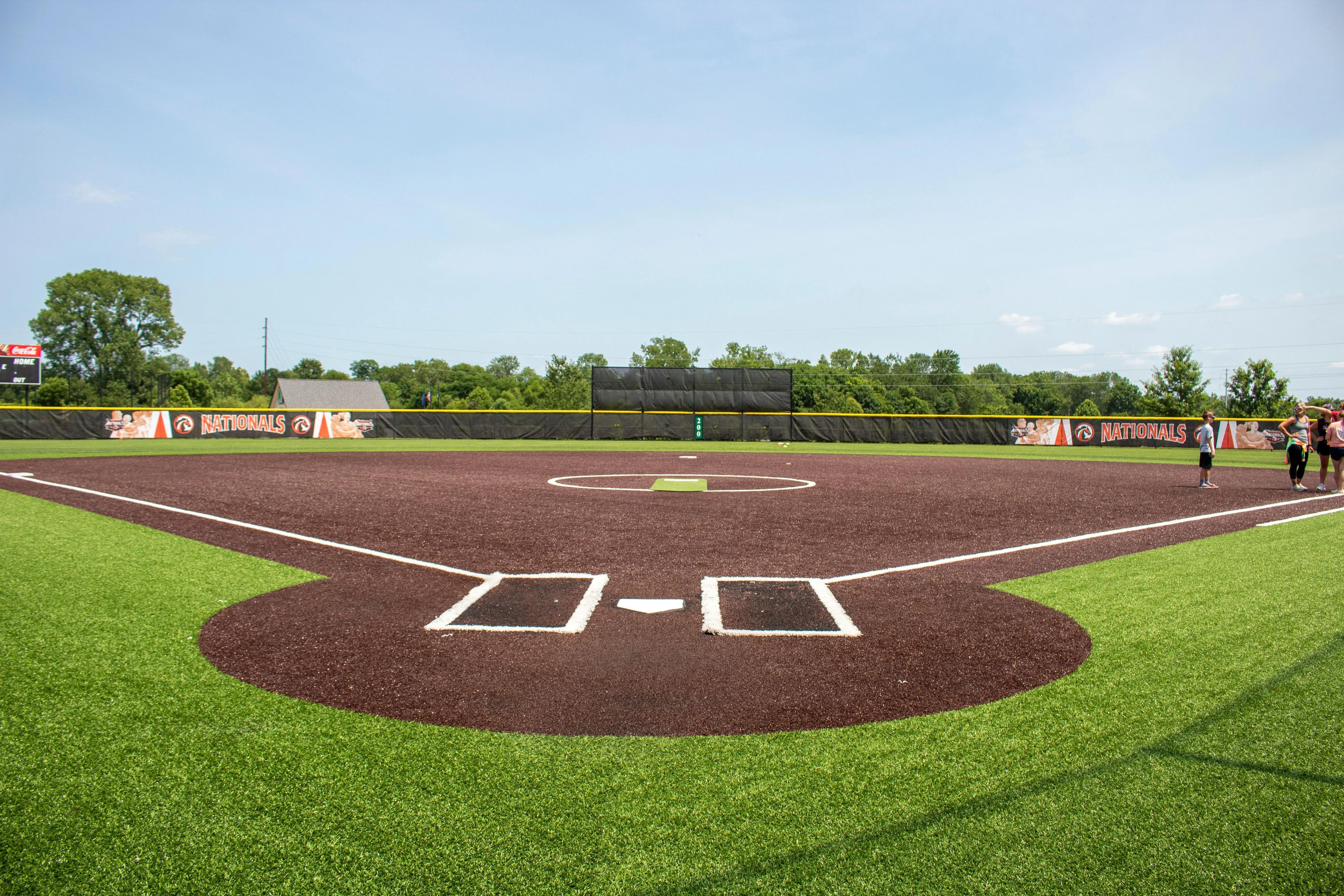 Finished youth baseball field with artificial turf infield and green outfield, view from behind home plate