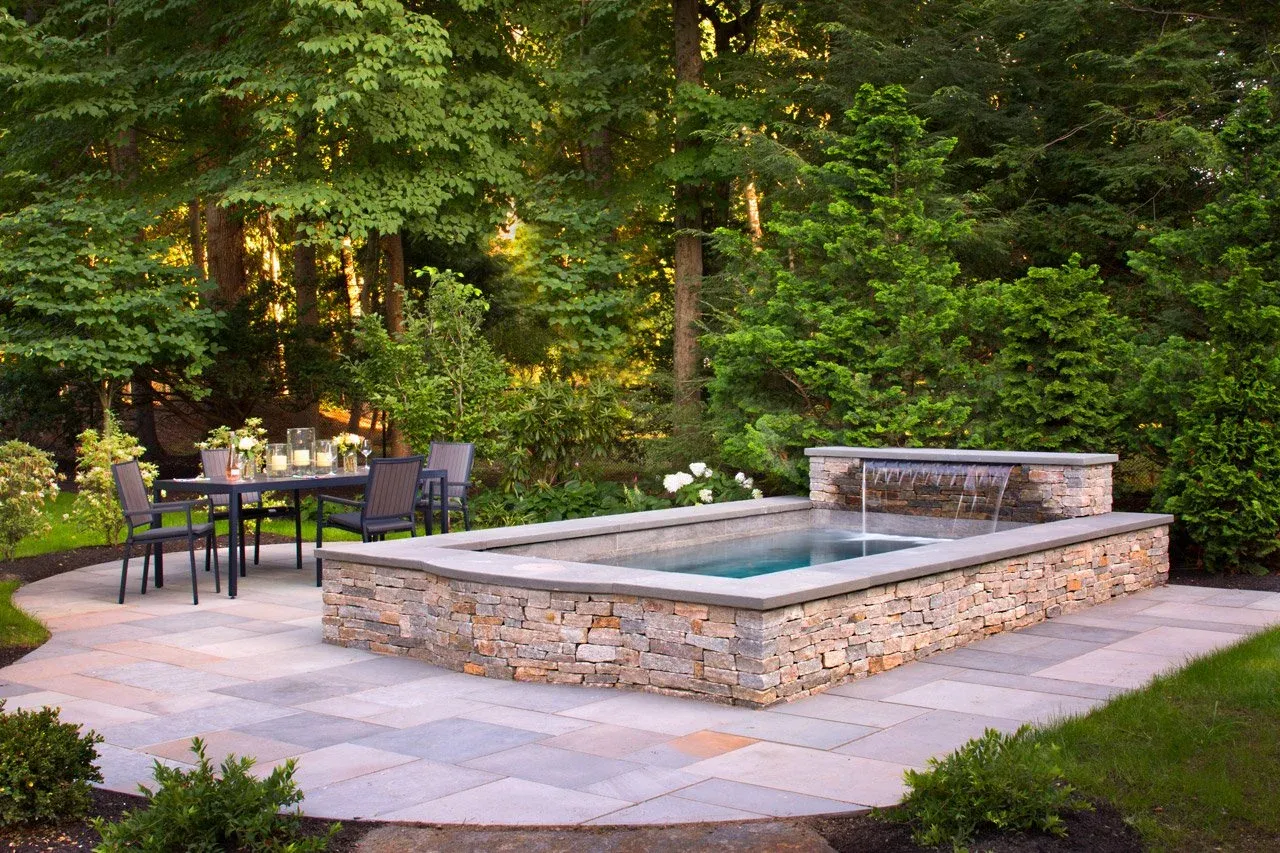 Soake precast plunge pool with a stacked-stone raised surround, sheet waterfall, and bluestone patio